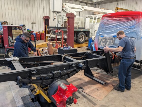 Two people working on a truck frame in a mechanic shop.